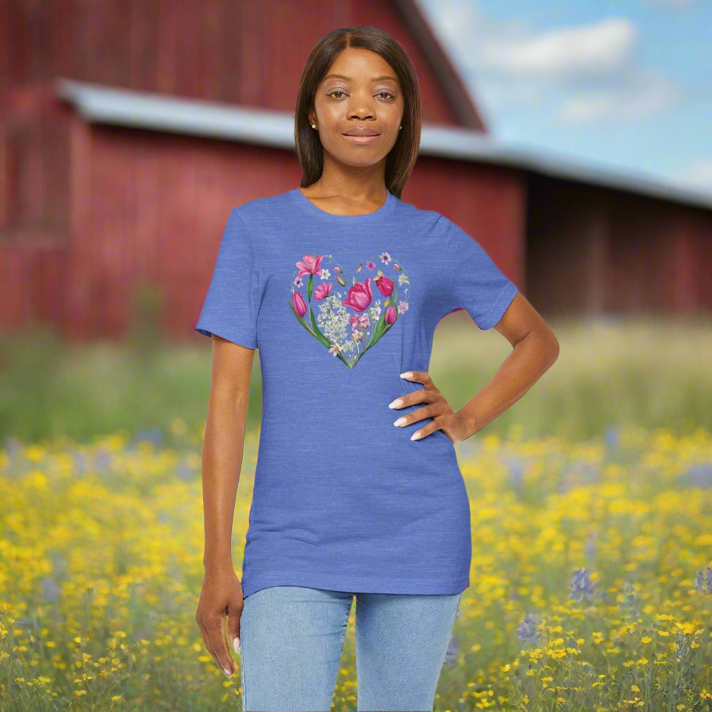 Heart of Flowers Short Sleeve Adult Tee. Girl, hand on hip in a blue short sleeve t-shirt with image of wildflowers in the shape of a heart. Old red barn in a field of wildflowers in background. 